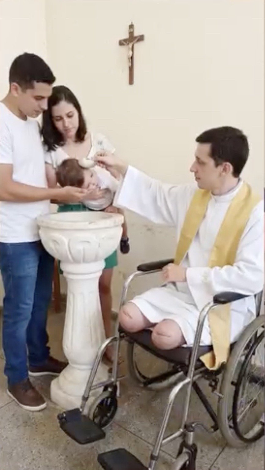Padre Miguel realizando um batismo sentado na cadeira de rodas